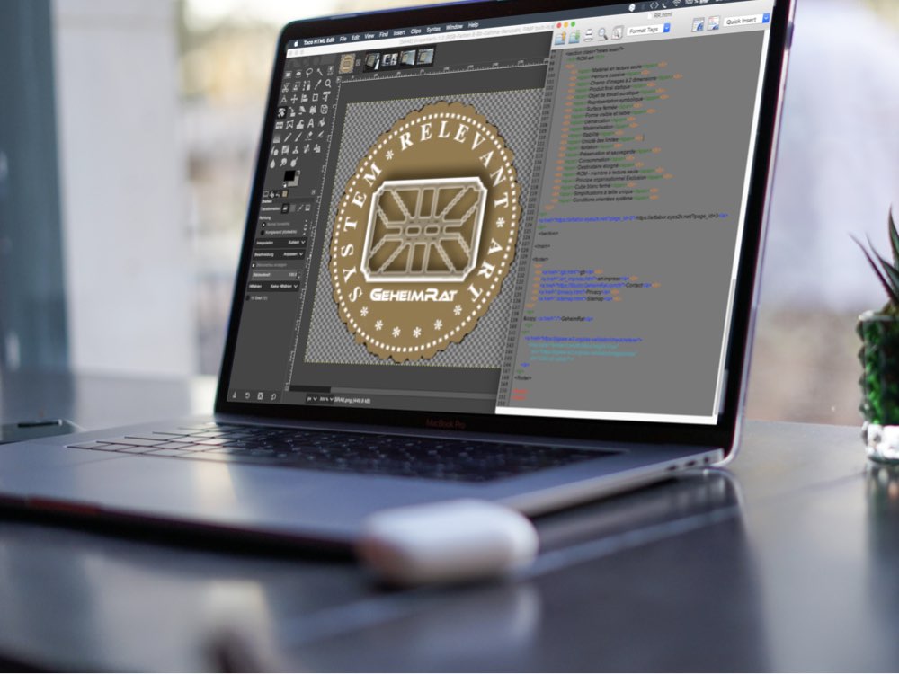Vue de l'écran d'un ordinateur portable. Sur l'écran, on peut voir un emblème de couleur dorée ouvert dans un éditeur graphique, avec 'System Relevant Art' et 'GeheimRat' écrits dessus. À droite, on peut voir un fichier html ouvert dans un éditeur html.